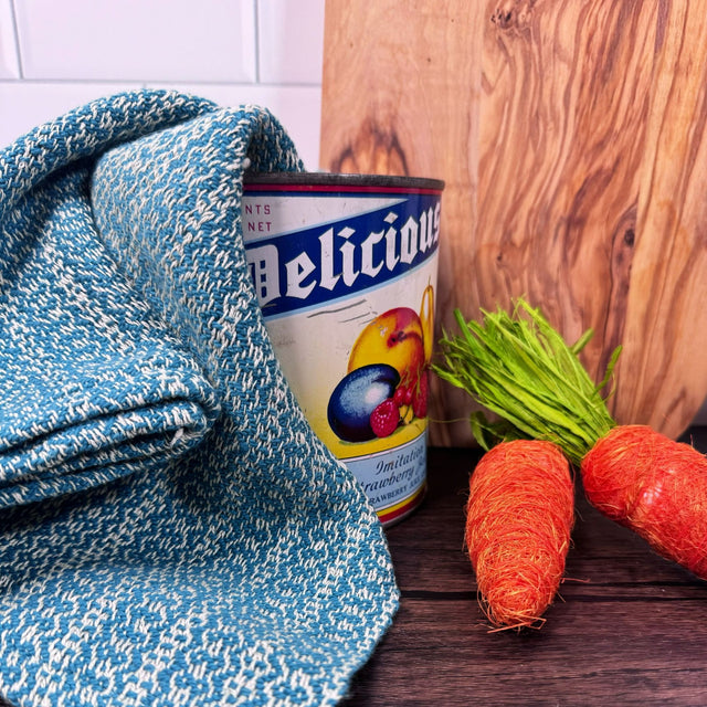 Dark Teal and white honeycomb design dish towels- hand woven hemp and cotton blend. Pictured on a brown table, draped over an antique can, with a wooden cutting board in the background and carrots on the side.