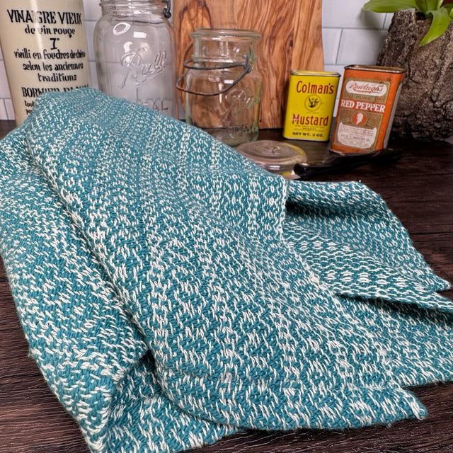 Dark Teal and white honeycomb design dish towel - hand woven hemp and cotton blend. Pictured on a brown table, with a plant, two antique cans, and two mason jars in the background..