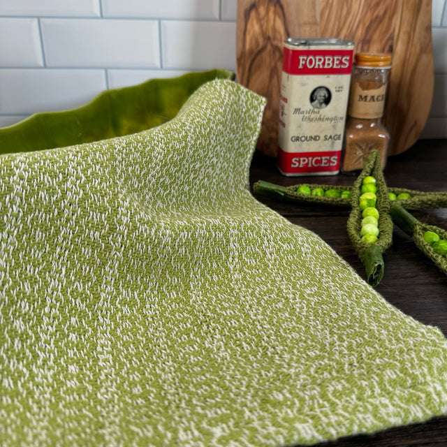 Lime Green and white honeycomb design dish towel - hand woven hemp and cotton blend. Pictured on a brown table, a cutting board, two spice jars, and snap peas in the scene.