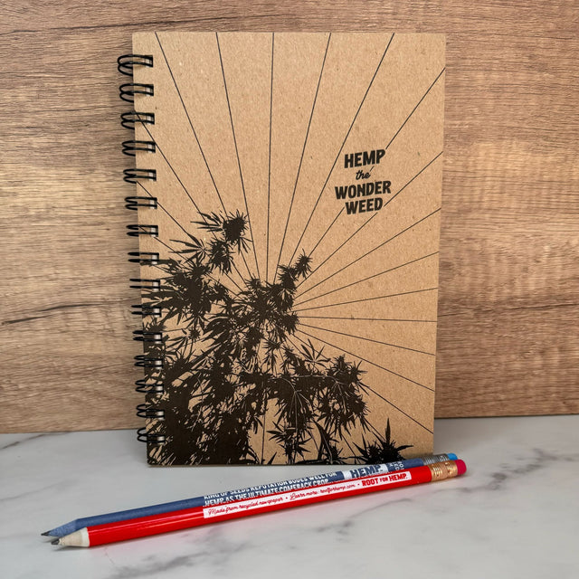 hemp paper wonderweed sketchbook with natural cover. Print on cover is hemp plant, sun rays and words "hemp the wonderweed" in all black font. one red and one blue pencil.