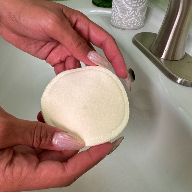 Woman's hands holding a single hemp facial round over a sink. A faucet and soap dispenser can be seen in the background.