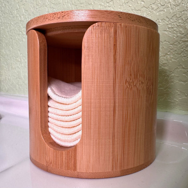 Cylindrical Bamboo box with hemp facial rounds stacked inside. Box has a slit opening down the side for dispensing. Box is on a white counter top with green wall background.