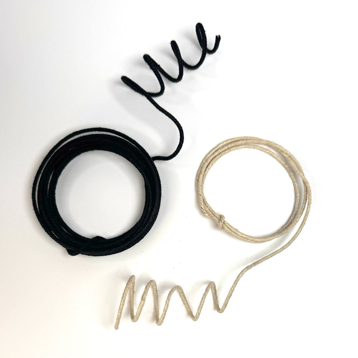 On the left is black wire hemp cord wound into a circle the end unwound but in a spiral. On the right is natural color wire hemp cord wound into a circle the end unwound but in a spiral.
