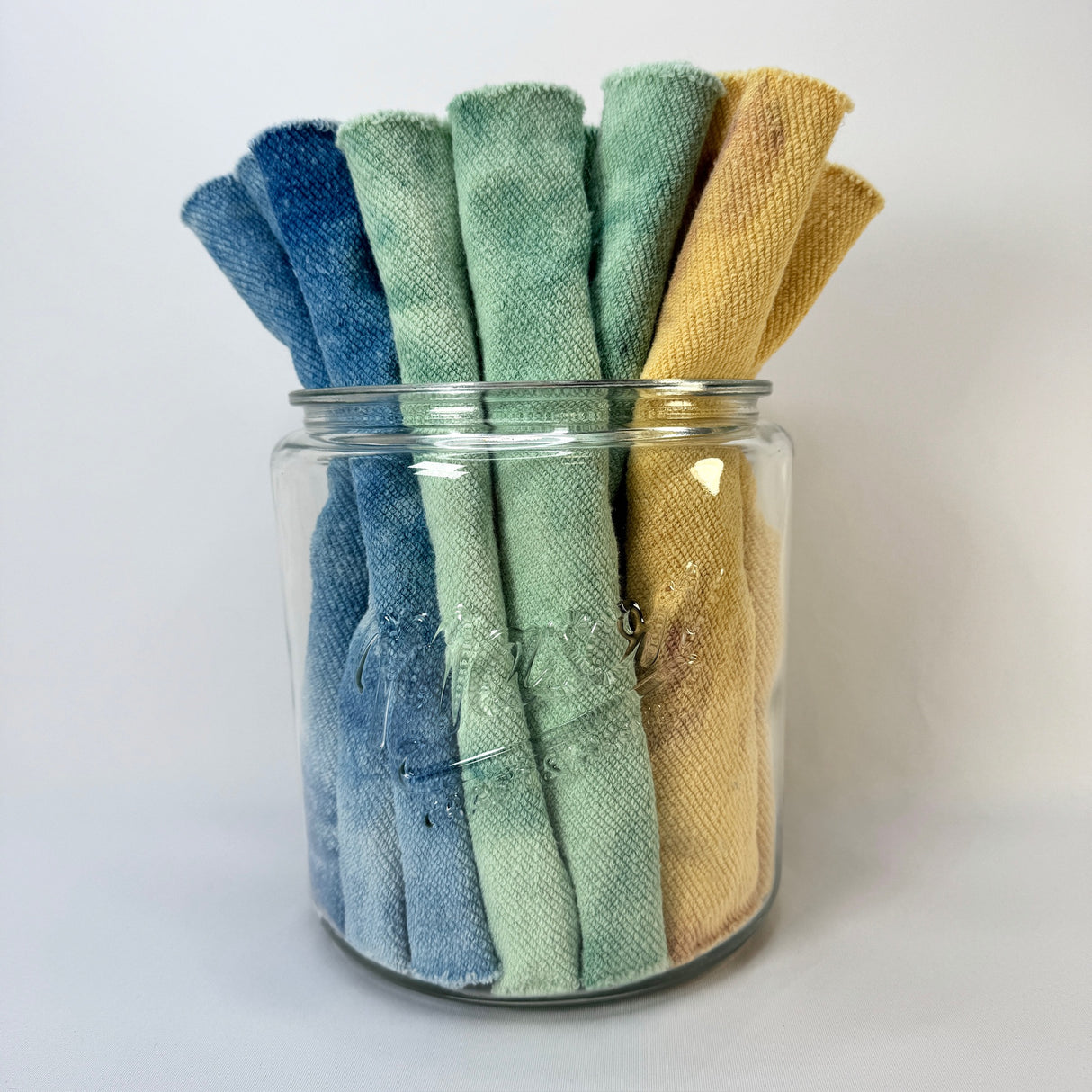 Set of colorful rolled towels in a glass jar on a white background