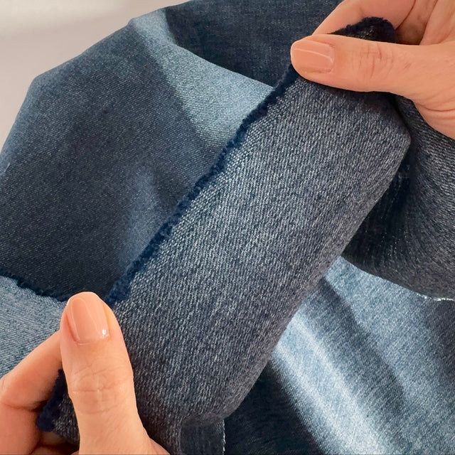 Close-up of hands holding and manipulating a piece of blue denim fabric.