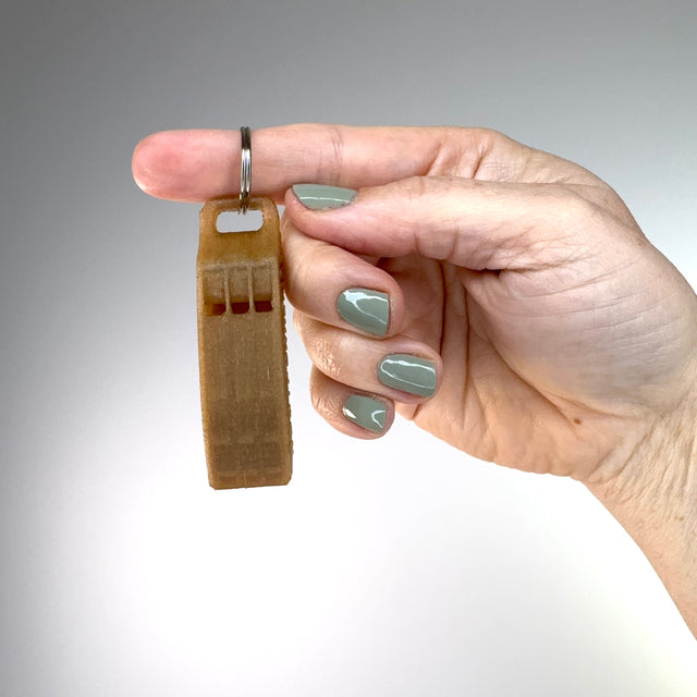 Hand holding a small brown whistle keychain against a gradient gray and white background