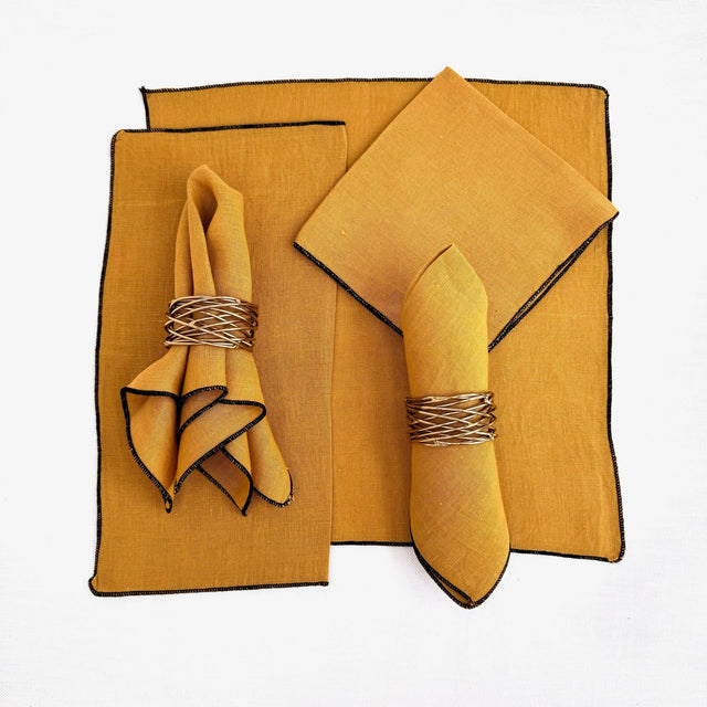 100% hemp mustard color table napkin pictured with 5 different ways to fold the napkin.  Napkins have black threading on the edge.