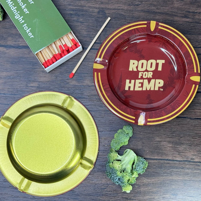 Bottom viewof the ash tray - bottom is gold. Top view of the ash tray which Red and gold with dark red leaf pattern, "Root for Hemp". Also pictured with a book of matches and chopped broccoli.