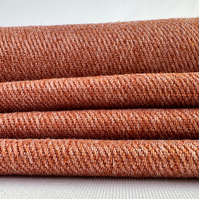 Stack of terra cotta hemp twill fabric rolls on a white background