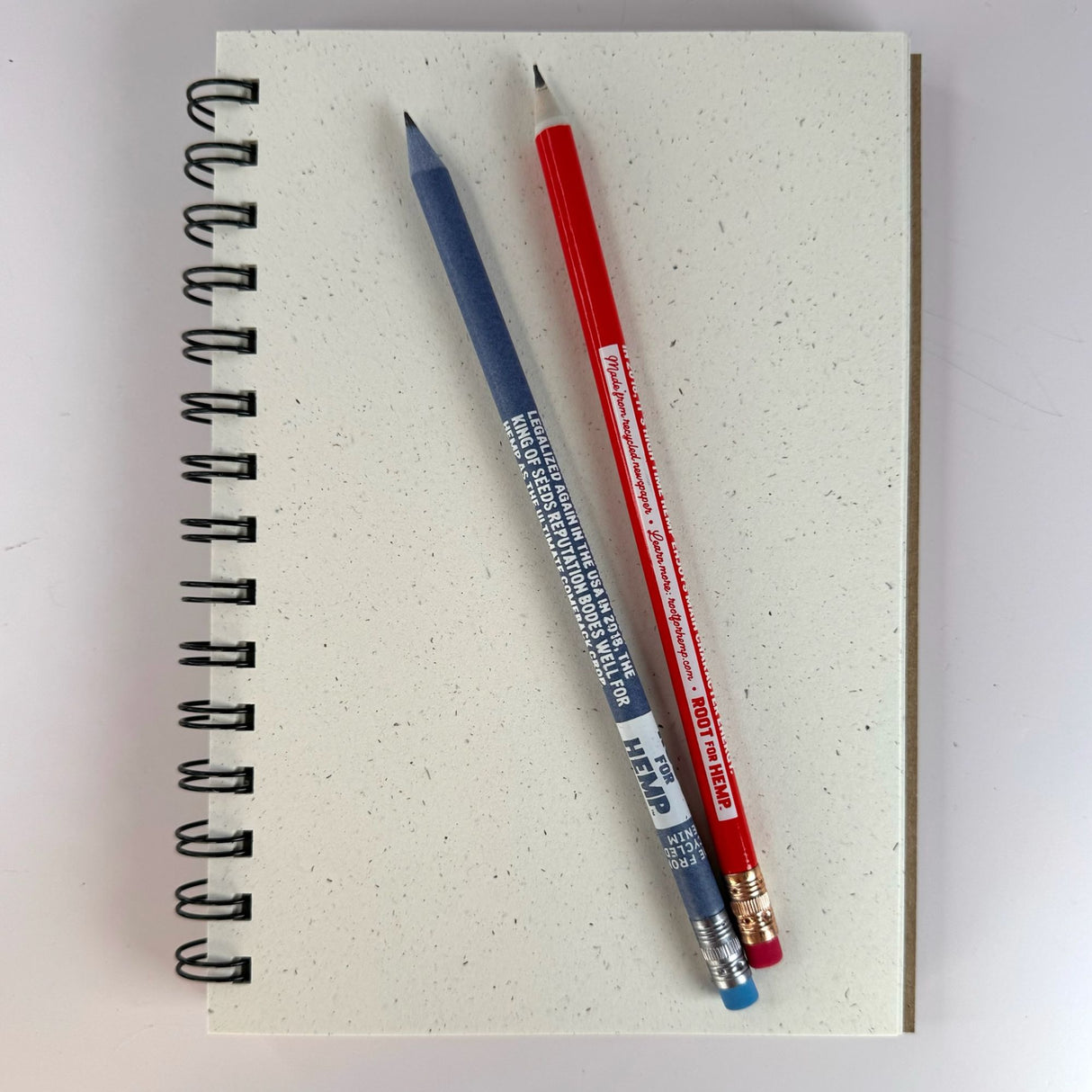 Hemp paper unlined sketchbook with spiral wire binding opened with two sharpened pencils. One pencil is red and the other is blue