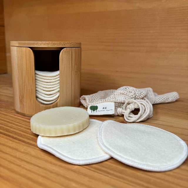 Cylindrical Bamboo box with hemp facial rounds stacked inside. Box has a slit opening down the side for dispensing. Also pictured with two facial rounds outside the box along with a mesh washing bag.