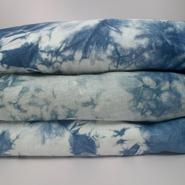 Closeup view of three folded indigo tie dye hoodies. Picture shows the uniqueness of the dye pattern on each unit.