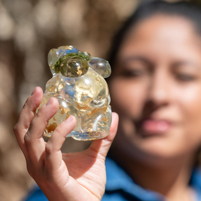 Resin pachamama with filled with hemp leaves and gold flakes in the hand of a woman. Woman's face can been seen blurry in the background.