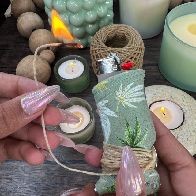 Closeup view of a toker poker that is light green with hemp leaves printed in yellow, green and white.  Toker is wrapped with hemp wick and pictured with candles and beads in the background.