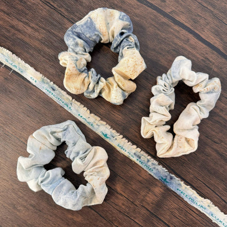 Three blue eco print hemp scrunchies, pictured on a dark wooden table and pictured with a piece of hemp fabric scrap of the same fabric that reads "100% hemp"