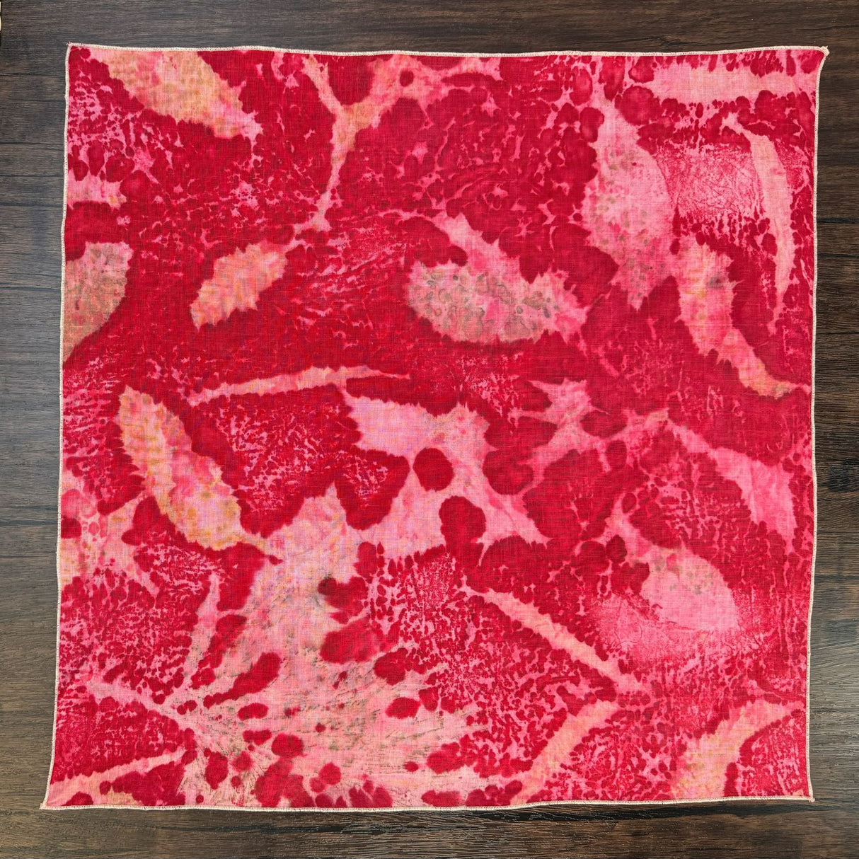 Unfolded view of the red eco print hemp bandana, pictured on a dark wooden table.