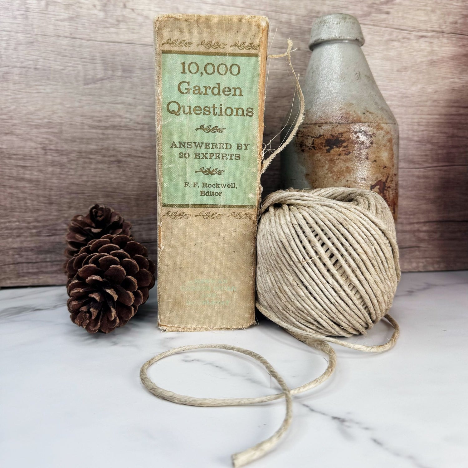 A roll of thick hemp garden cord pictured on a white marble surface with pine cones and antiques in the background. 