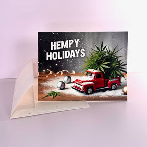 A greeting card with a red toy truck filled with hemp, indicating a Hempy Holidays theme. The card is presented against a neutral background.