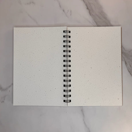 Open book view of hemp paper sketchbook with unlined paper.  Spiral wire binding can be seen between left and right pages.