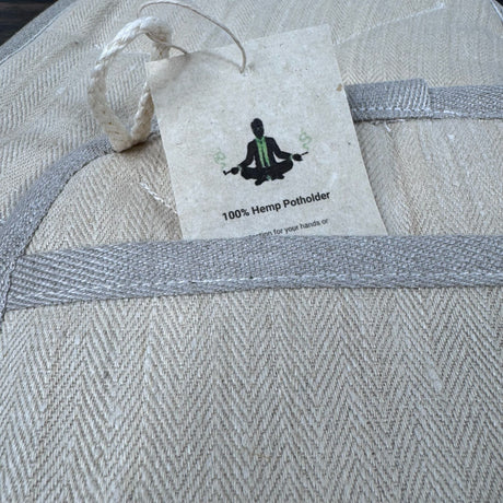 Closeup view of the picket of the hemp potholder - natural color with grey edging.  The Maker tag is visible with the words "100% hemp potholder"