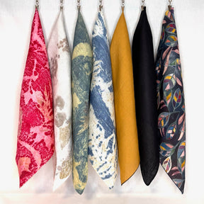 A selection of hemp bandanas in various colors and patterns displayed hanging against a white background.