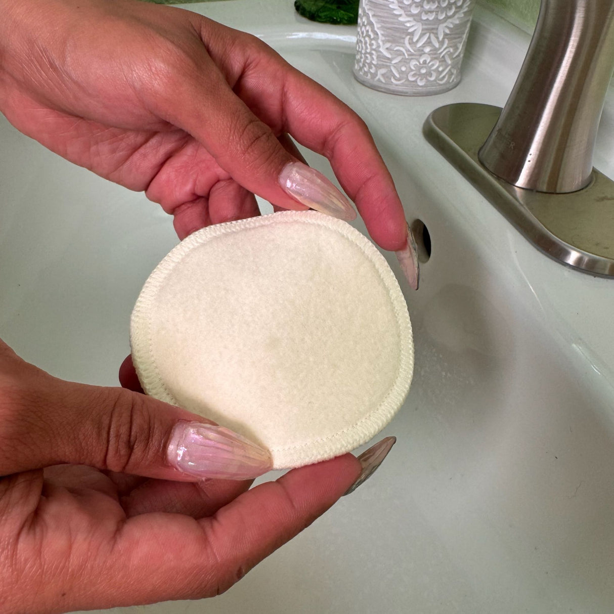 Woman's hands holding a single hemp facial round over a sink.  A faucet and soap dispenser can be seen in the background.