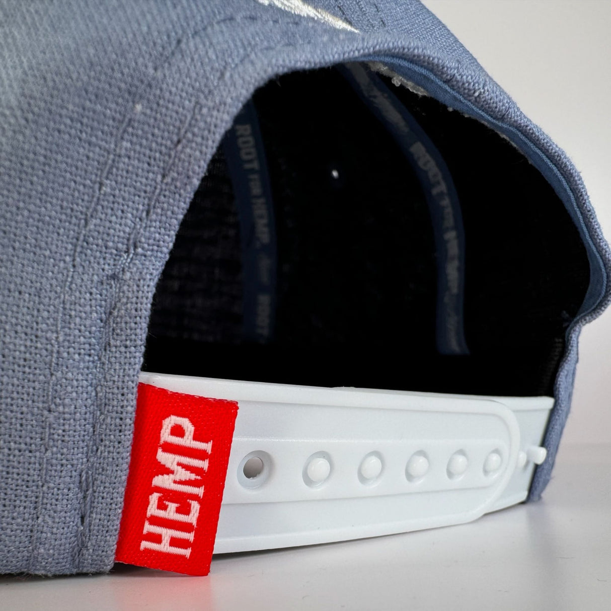 Closeup view of the back of the hemp vote hat - white snapback with a red tag that says HEMP in white letters.  You can also see the inside of the hat and the ribbing that is branded with "Root for Hemp."