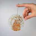 Hand holding a round decorative item with natural elements fiber fabric seeds on a gray background