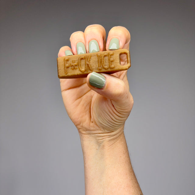 Hand holding a hemp whistle with "F*CK ICE" against a gray background