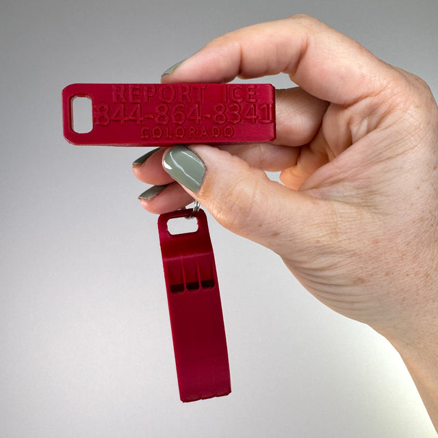 Red whistle with Colorado Hotline held by a hand against a gray background