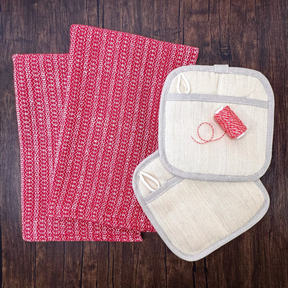 A set of handwoven dish towels in red, a set of beige hemp potholder, and a spool of hemp baker's twine on a wooden surface.