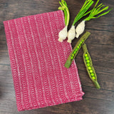 Red and white honeycomb design dish towels hand woven hemp and cotton blend.  Pictured on a brown table with green onions and snap peas.