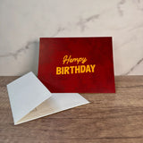 Red hemp paper greeting card with yellow words that read "hempy birthday." Pictured with an unsealed hemp paper envelope.