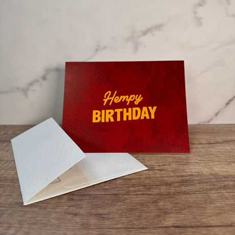 Red hemp paper greeting card with yellow words that read "hempy birthday." Pictured with an unsealed hemp paper envelope.