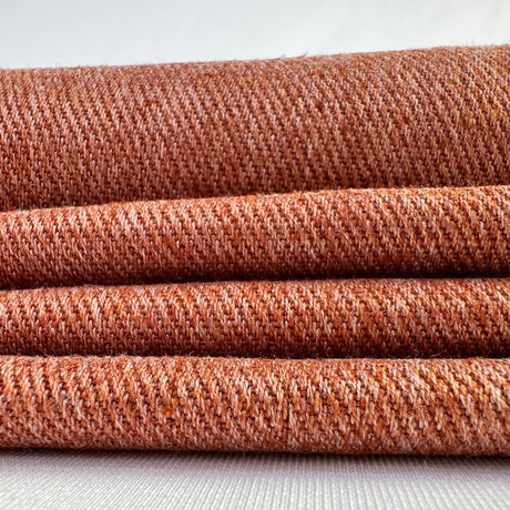 Stack of terra cotta hemp twill fabric rolls on a white background