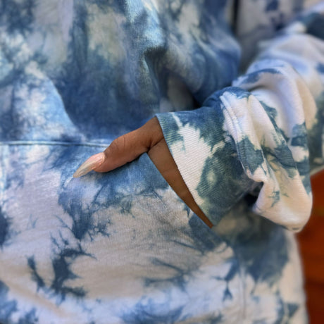 Closeup view of model wearing an indigo tie dye sweatshirt to show the front pocket view.  Model has her hand partially in the pocket.  