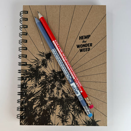 sketchbook with hemp the wonder weed printed on the front along with a hemp plant.  Sketchbook has a wire binding.  Pictured with two pencils sitting on top - one red and one blue.