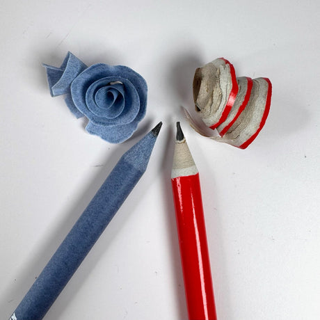 two sharpened pencils pictured next to the sharpening debris coiled up.  One pencil is red and the other is blue.  pictured on a white background