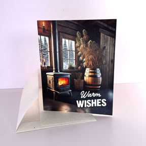 Winter greeting card that reads "warm wishes" with wood burning stove and barrel of hemp, with natural speckled enelope