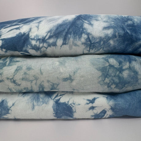 Closeup view of three folded indigo tie dye hoodies. Picture shows the uniqueness of the dye pattern on each unit. 