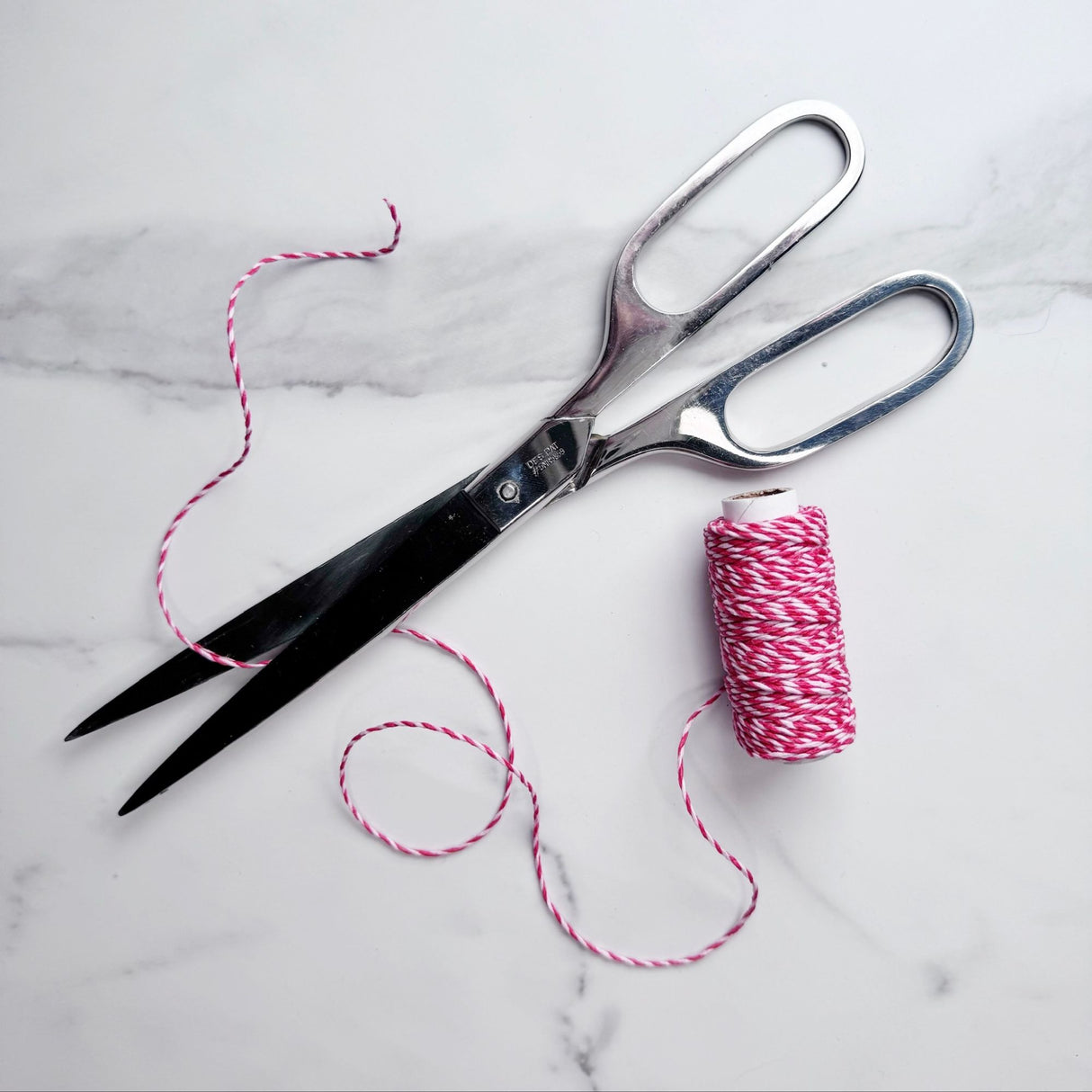 Red and white spiral hemp cord partially unwound on a white marble table, pictured with classic silver colored scissors.