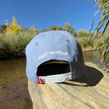 Back view of a Blue hemp vote baseball hat with a white snapback with a small red tag that says "hemp" and the words "root for hemp embroidered on the back. 
 Pictured outside on green grass with some yellow leaves and a river in the background. 