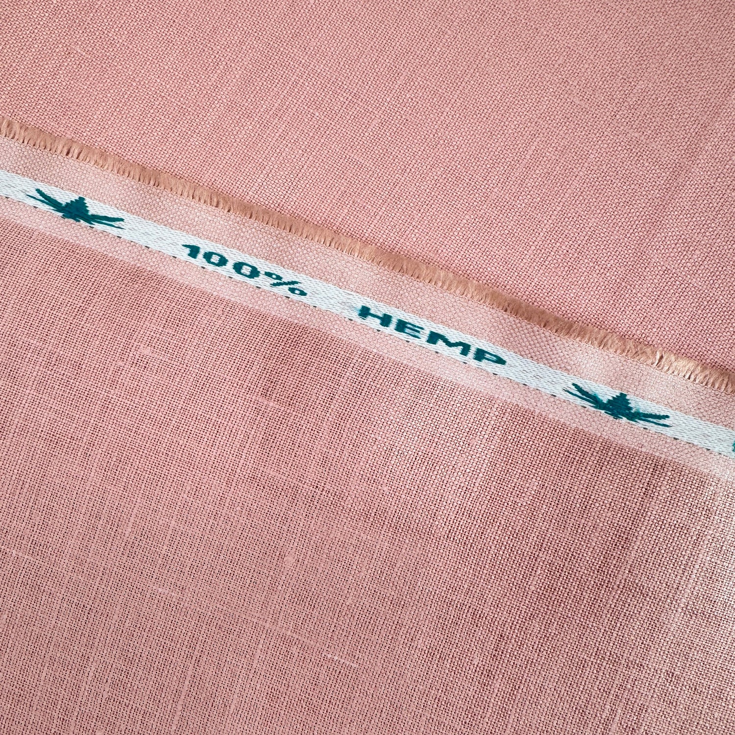 Close-up of pink fabric with a white stripe displaying '100% Hemp' text.