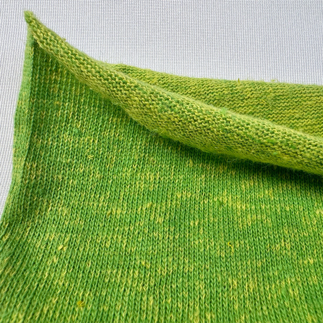 Close-up of green knitted fabric with a subtle pattern on a light gray background
