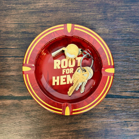 Round metal ash tray with red and gold with dark red leaf pattern, "Root for Hemp" on center of dish, show as being used as a key dish - holding a set of three keys and a whistle.