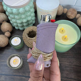 Plum colored toker poker with hemp wick wrapped around the bottom of it.  Pictured on a dark wooden surface with candles, beads, and a roll of hemp wick in the background.