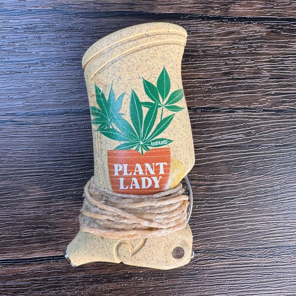 Closeup view of a toker poker that is yellow/brown with the words "plant lady" printed on the front along with a picture of hemp leaves coming out of a planting pot.   Toker is wrapped with hemp wick and pictured on a wooden surface. 