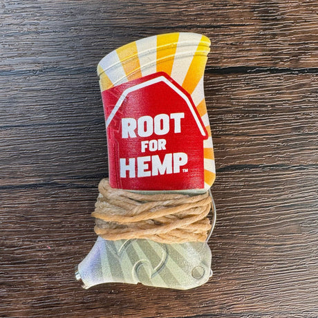 Closeup view of a toker poker with the words "root for hemp" in white text on a red barn.  There are yellow sunburst and green fields also in the design.  Toker is wrapped with hemp wick and pictured on a wooden surface. 